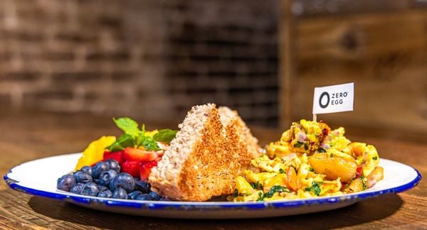 左边的盘子里有蓝莓和草莓,右边的盘子里有一个三角形的吐司,中间少了一口,右边的盘子里有一个蔬菜炒鸡蛋,上面插着一根Zero egg牙签。