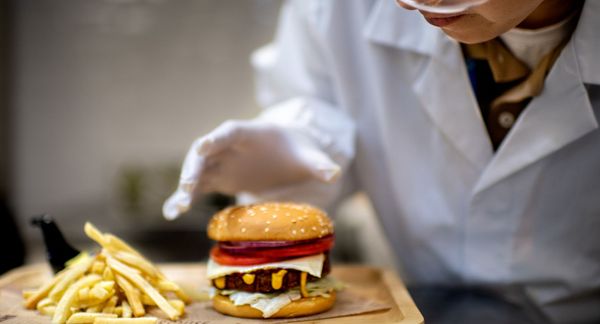 一个穿着白大褂、戴着护目镜的人目不转睛地盯着一个植物性汉堡和薯条。