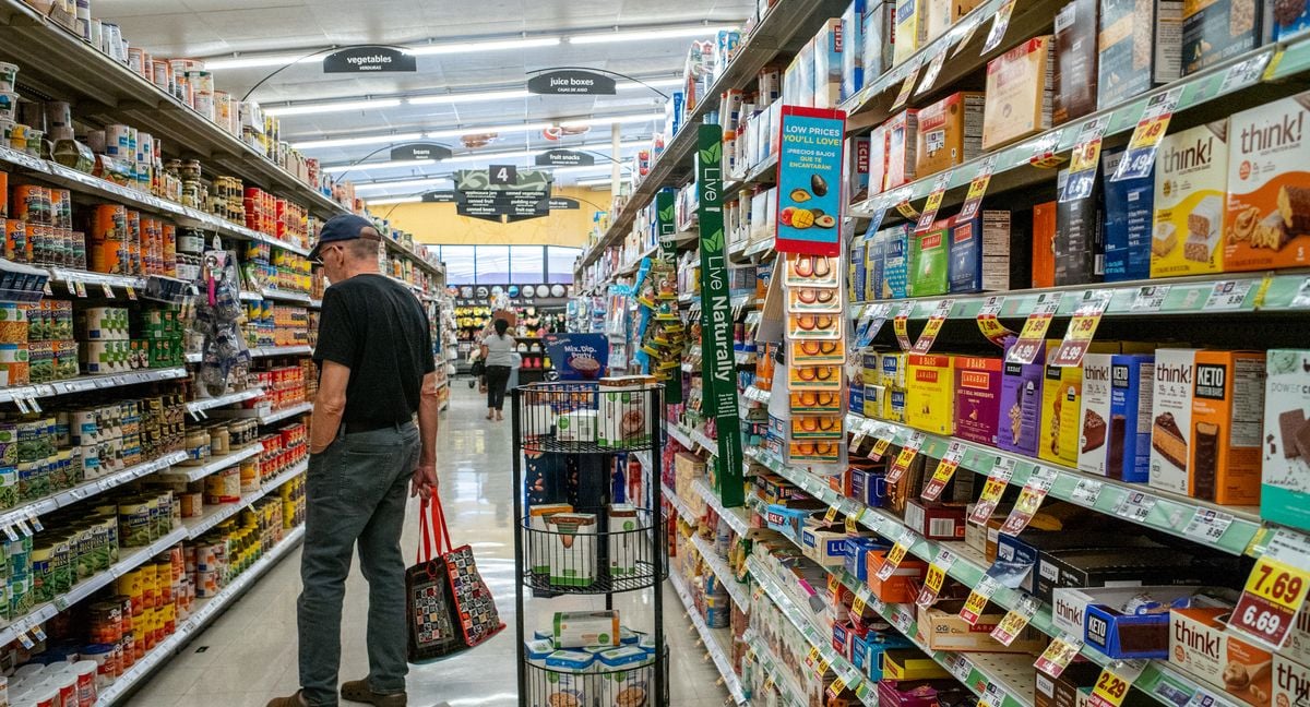 A person carrying a tote bag looks at items on a grocery store shelf