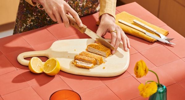 一个人在珊瑚色的柜台上的白色砧板上切肉片。＂loading=