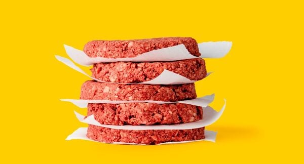 一堆未煮熟的不可能的汉堡肉饼，用蜡纸在黄色背景上分开