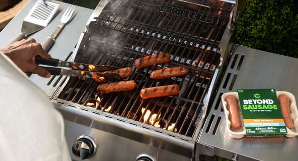 一个人在室外烤架上烹饪Beyond sausage，包装在右侧。