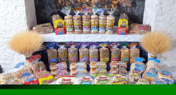 爸爸皮塔面包店的小圆面包、面包、百吉饼、英式松饼、玉米饼和大饼摆放在白色的砖架子上，背景是小麦捆。