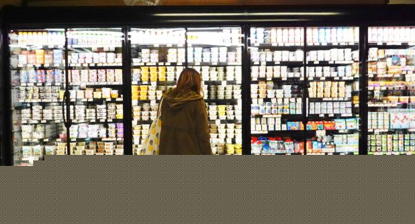 在一家杂货店，一个人推着购物车站在一排装满食物的冰箱前。