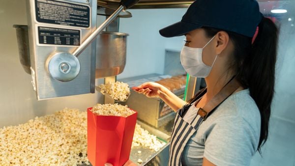 Woman working at a concession stand selling popcorn at the movie theater wearing a facemask